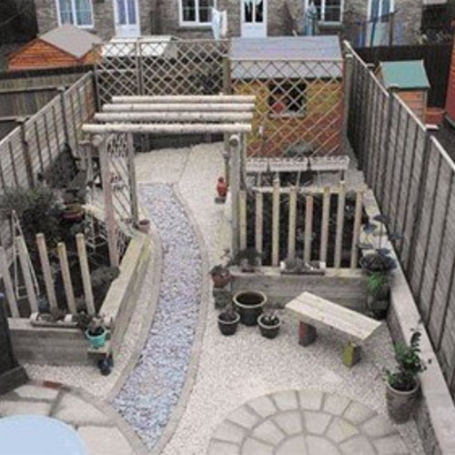 An aerial shot of a landscaped garden featuring a stone circle and winding paths, a rustic wooden pergola and raised wooden beds full of shrubs backed by trellis for privacy